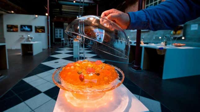 Person lifts glass lid off of orange Jell-O salad ring