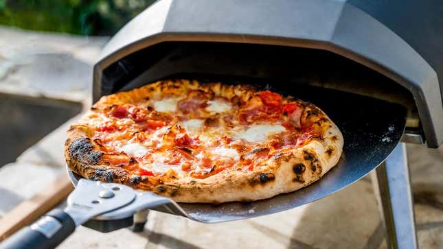 Homemade pizza being pulled from outdoor portable pizza oven